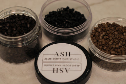 Three small containers with hair extensions and a branded lid on a light surface.