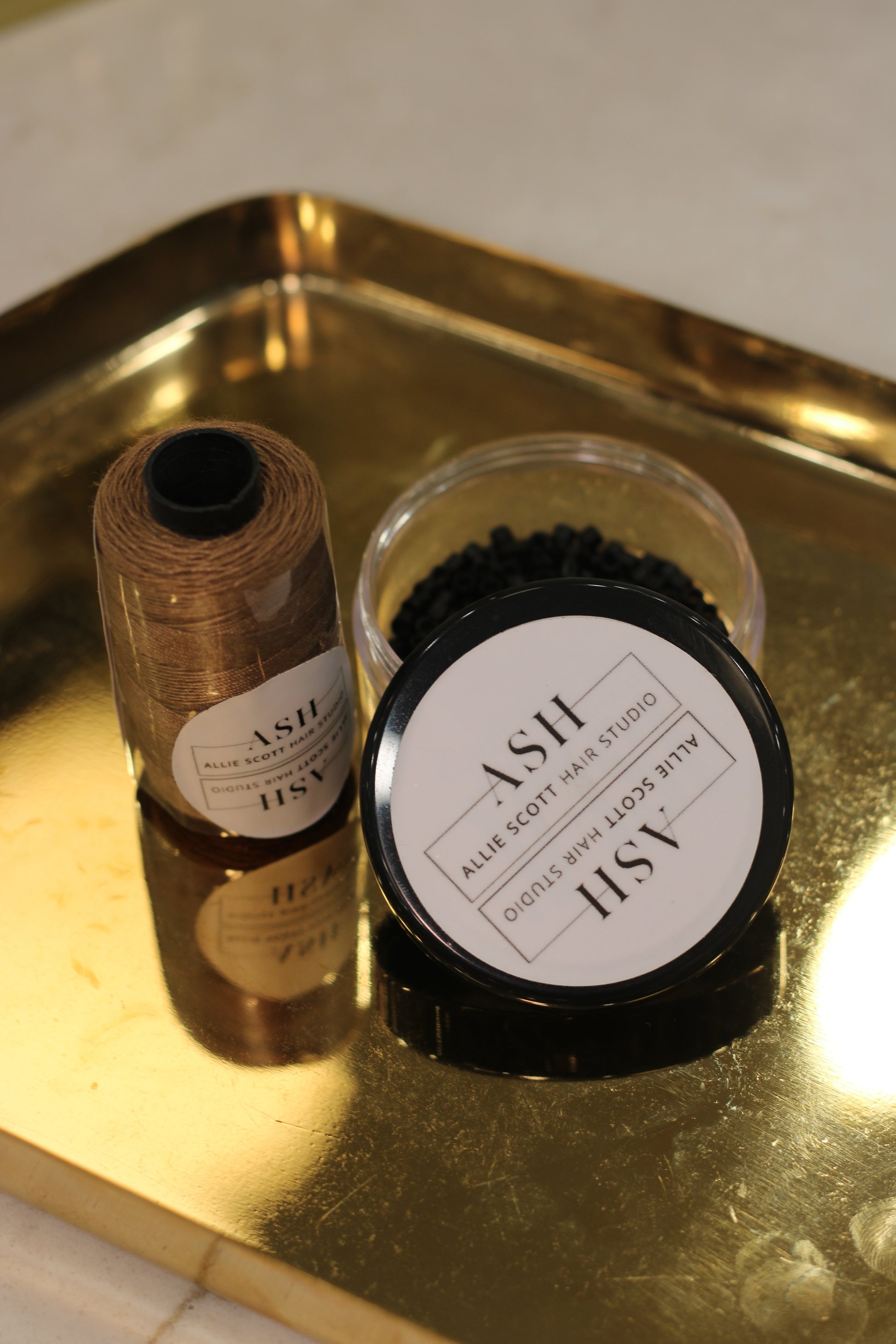 Two spools of thread labeled 'ASH' on a reflective gold surface.
