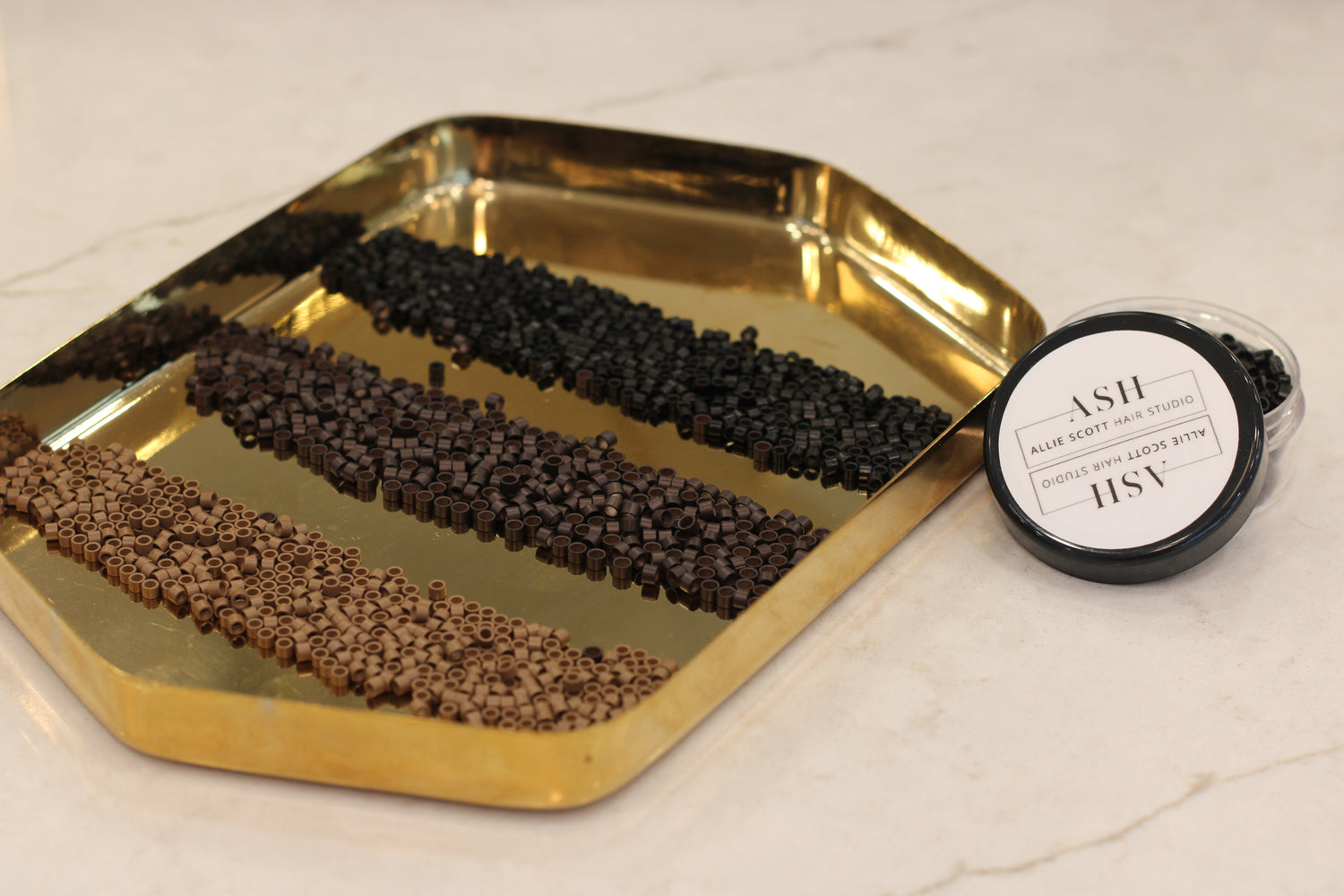 Gold tray with black and brown beads and a container on a light background