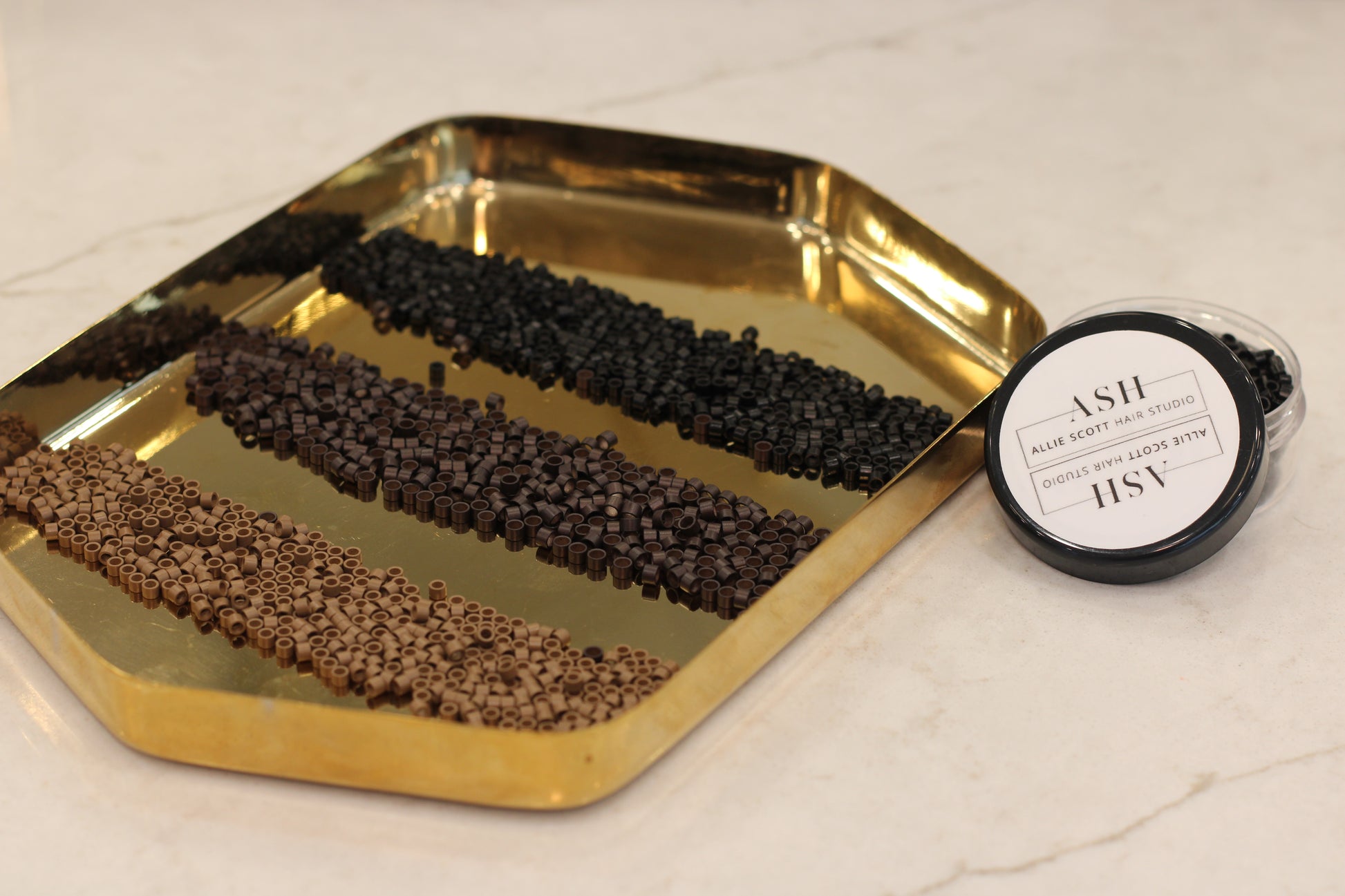Gold tray with black and brown beads and a container on a light background