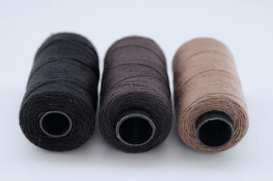 Three spools of thread in black, brown, and beige on a white background